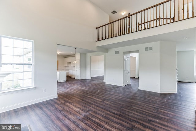 unfurnished living room featuring a high ceiling, plenty of natural light, and dark wood-type flooring