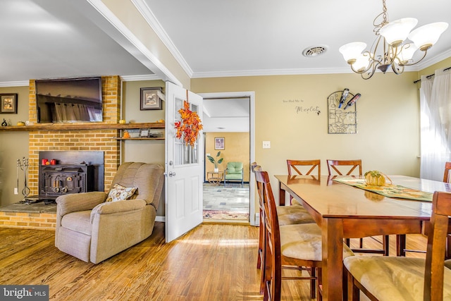 dining room featuring light hardwood / wood-style floors, a wood stove, crown molding, and a chandelier