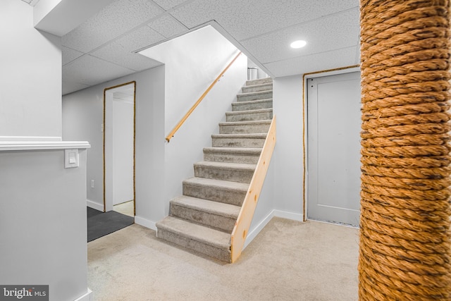 stairs with carpet floors and a paneled ceiling