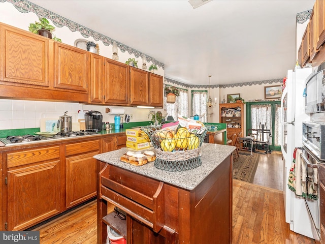 kitchen featuring stainless steel gas cooktop, light stone counters, hanging light fixtures, light hardwood / wood-style floors, and backsplash