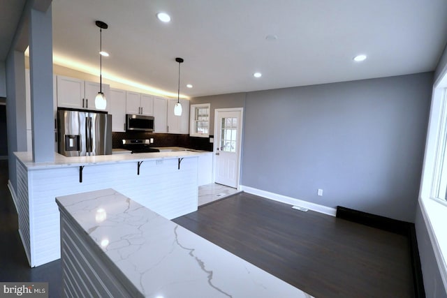 kitchen with white cabinetry, hanging light fixtures, stainless steel appliances, a kitchen breakfast bar, and dark hardwood / wood-style flooring