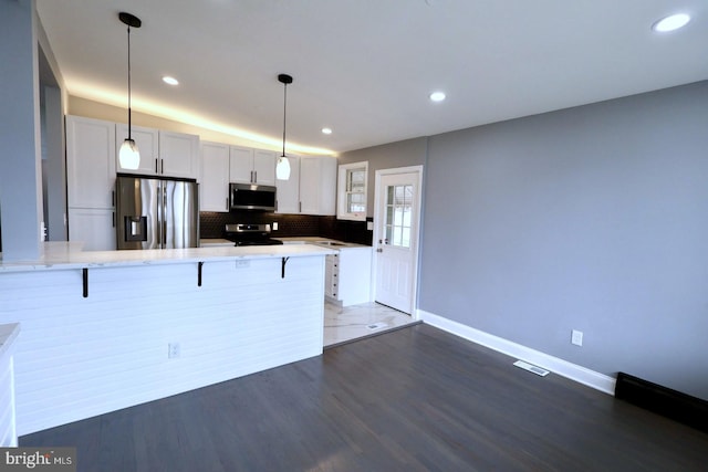 kitchen featuring appliances with stainless steel finishes, pendant lighting, white cabinets, dark hardwood / wood-style floors, and a breakfast bar area