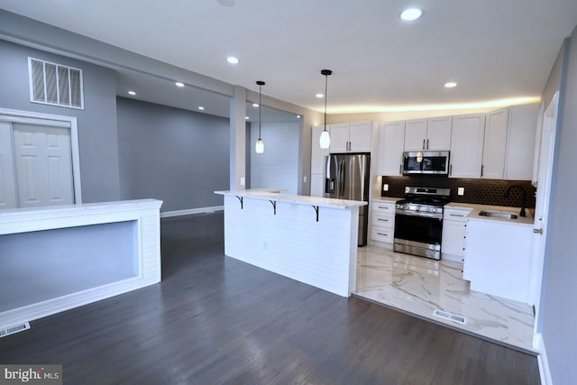 kitchen featuring appliances with stainless steel finishes, a kitchen breakfast bar, sink, pendant lighting, and white cabinets