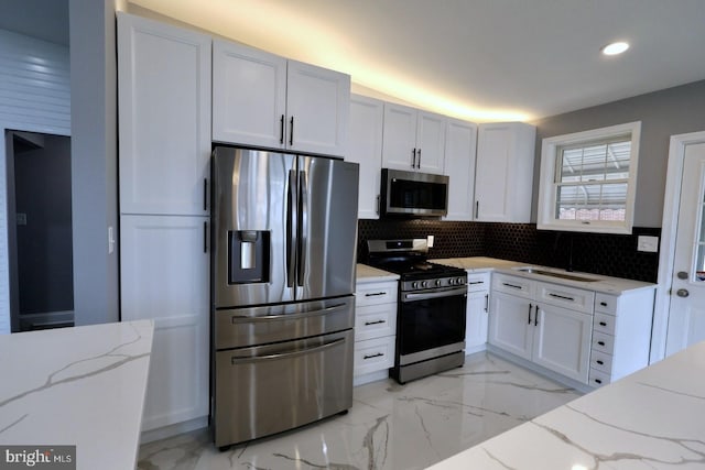 kitchen with sink, stainless steel appliances, white cabinetry, and light stone counters