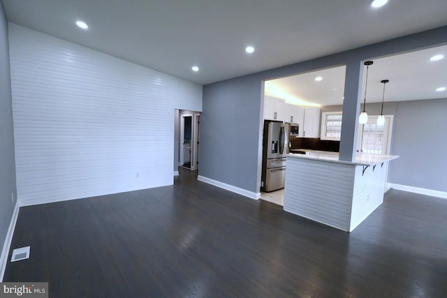 kitchen featuring kitchen peninsula, a kitchen breakfast bar, stainless steel refrigerator with ice dispenser, white cabinetry, and hanging light fixtures