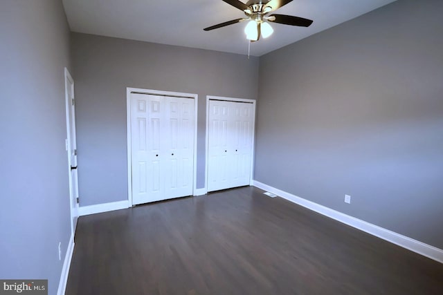 unfurnished bedroom with ceiling fan, dark hardwood / wood-style flooring, and two closets