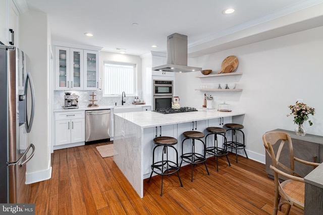 kitchen featuring island exhaust hood, kitchen peninsula, stainless steel appliances, hardwood / wood-style floors, and white cabinetry