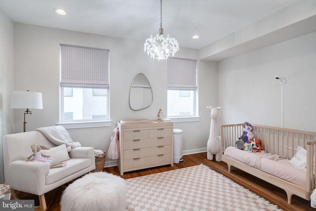 bedroom with hardwood / wood-style floors, an inviting chandelier, and a nursery area