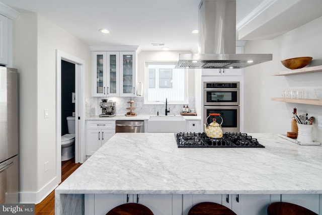 kitchen with decorative backsplash, a kitchen breakfast bar, appliances with stainless steel finishes, island range hood, and white cabinetry