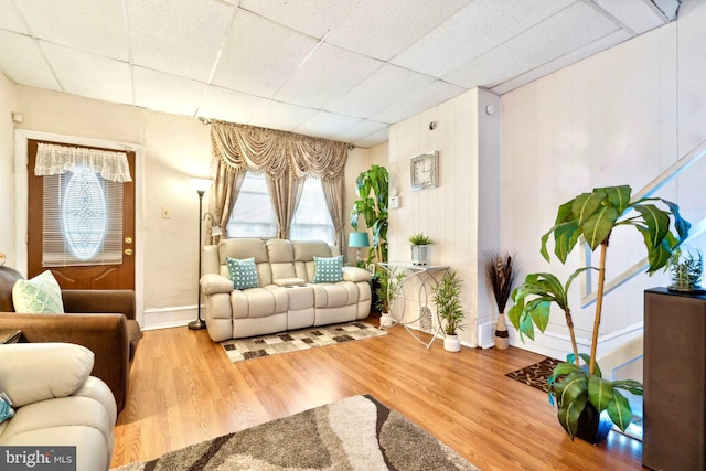 living room featuring wooden walls, a drop ceiling, and wood-type flooring