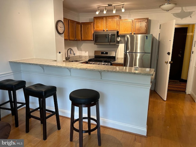 kitchen with sink, kitchen peninsula, crown molding, wood-type flooring, and appliances with stainless steel finishes