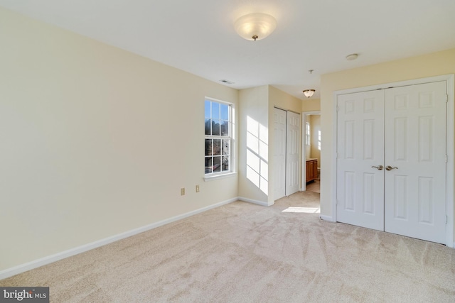 unfurnished bedroom with light colored carpet and two closets