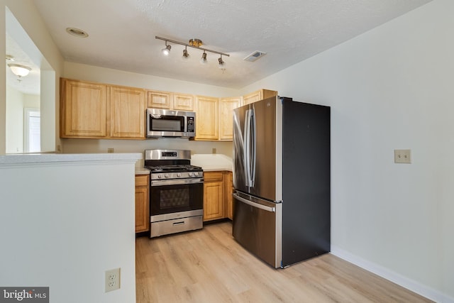 kitchen with light brown cabinetry, stainless steel appliances, a textured ceiling, and light wood-type flooring