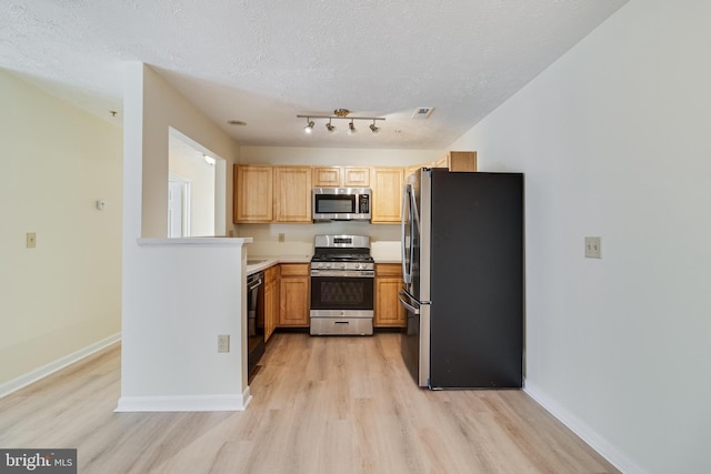 kitchen featuring light brown cabinetry, a textured ceiling, appliances with stainless steel finishes, and light hardwood / wood-style flooring