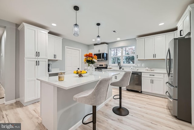 kitchen with white cabinetry, pendant lighting, stainless steel appliances, and light hardwood / wood-style floors