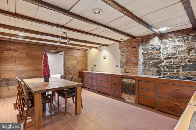 interior space with beamed ceiling, stainless steel gas cooktop, wooden walls, and light tile patterned flooring