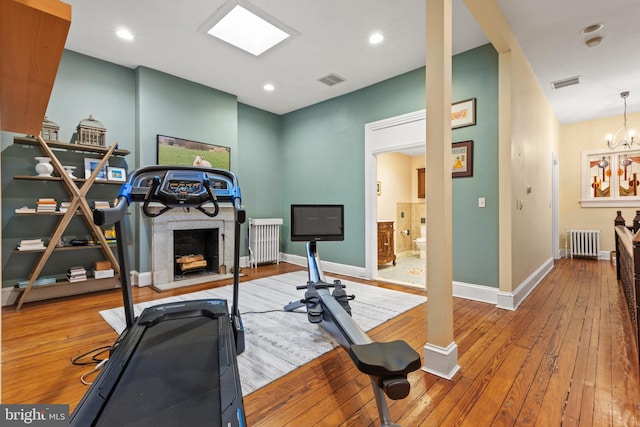 workout area featuring radiator heating unit, an inviting chandelier, and hardwood / wood-style flooring