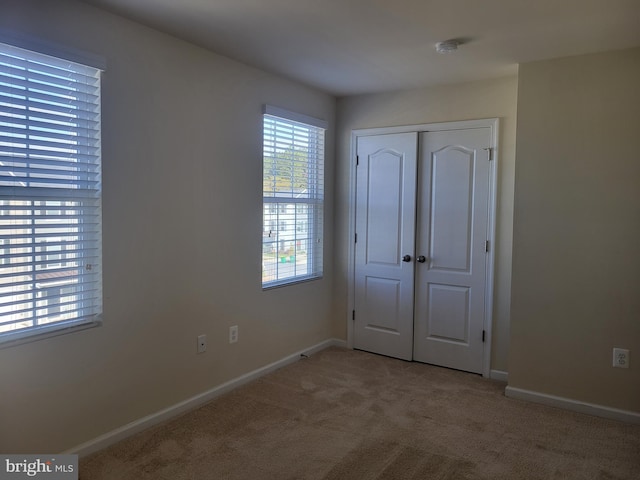 unfurnished bedroom with a closet, light colored carpet, and multiple windows