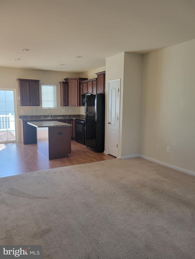 kitchen featuring a center island, black appliances, sink, light colored carpet, and dark brown cabinetry