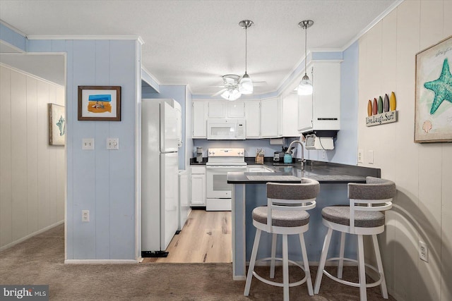 kitchen with kitchen peninsula, white appliances, sink, white cabinets, and hanging light fixtures