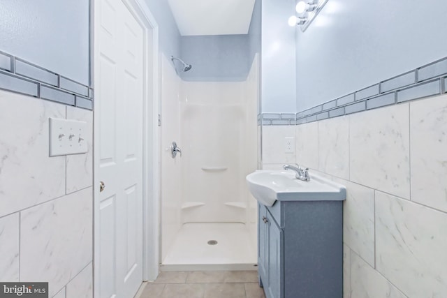 bathroom featuring tile patterned floors, vanity, a shower, and tile walls