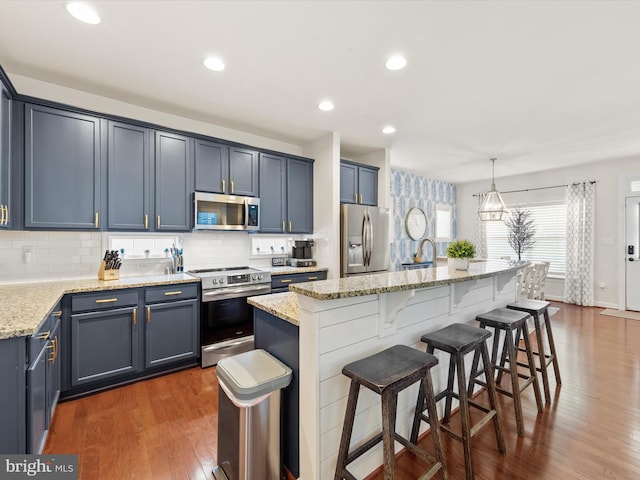 kitchen featuring dark wood-type flooring, a center island with sink, pendant lighting, and appliances with stainless steel finishes