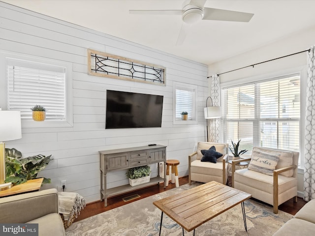 living room featuring wooden walls, ceiling fan, and wood-type flooring