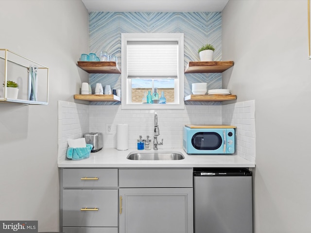 bar featuring gray cabinets, stainless steel dishwasher, and sink