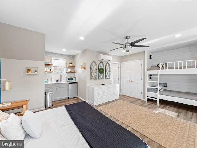 bedroom featuring a wall unit AC, ceiling fan, sink, and light wood-type flooring