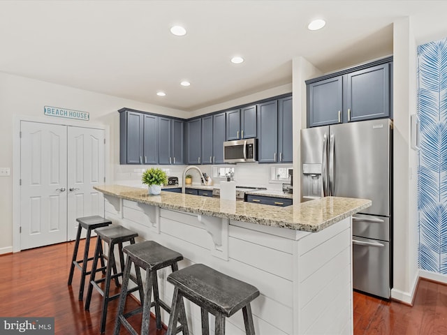 kitchen with a kitchen breakfast bar, stainless steel appliances, light stone counters, and an island with sink