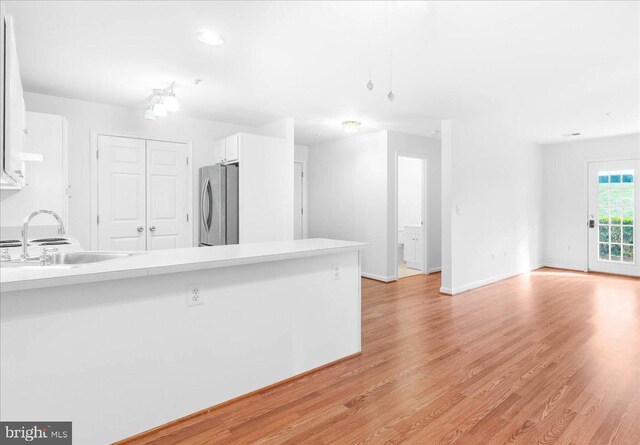 kitchen featuring sink, white cabinetry, light wood-type flooring, stainless steel refrigerator, and kitchen peninsula