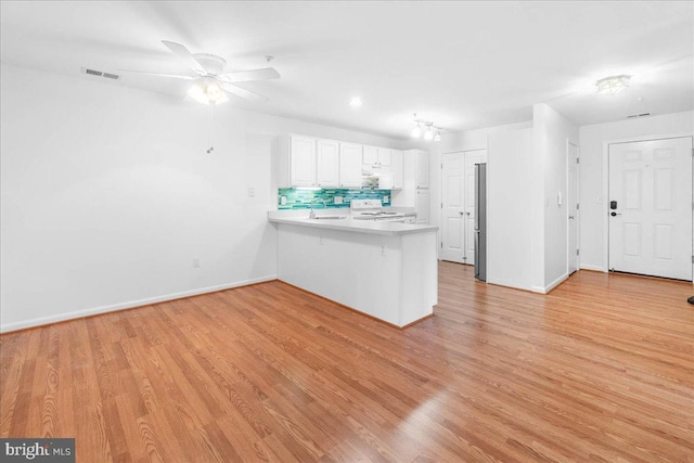 kitchen with light hardwood / wood-style flooring, white electric stove, kitchen peninsula, white cabinets, and backsplash