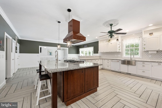 kitchen with island exhaust hood, white cabinetry, sink, and light stone countertops