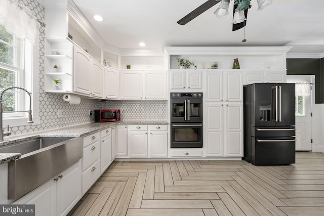 kitchen featuring white cabinets, black fridge, light stone countertops, and double oven