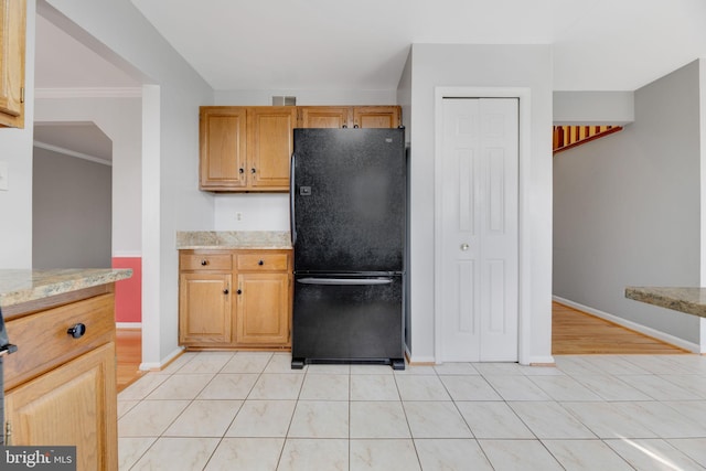 kitchen with crown molding, black refrigerator, light tile patterned floors, and light stone countertops