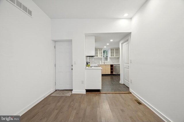 interior space with backsplash, sink, dishwasher, white cabinets, and hardwood / wood-style floors