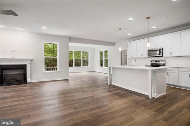 kitchen with stainless steel appliances, a center island with sink, white cabinets, dark hardwood / wood-style floors, and hanging light fixtures