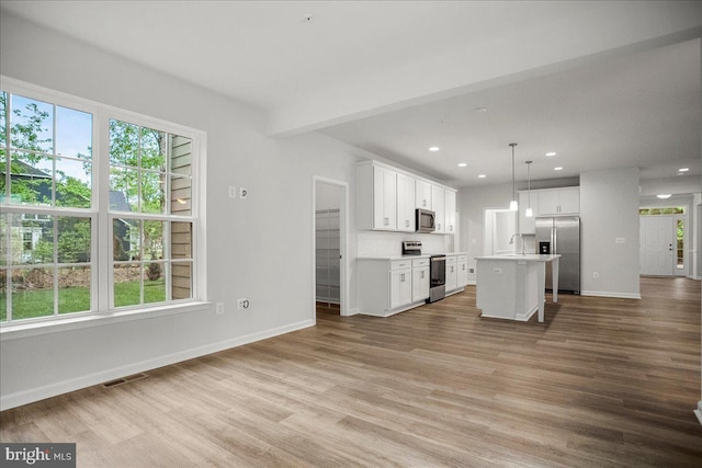 kitchen with a kitchen island, light wood-type flooring, decorative light fixtures, and appliances with stainless steel finishes