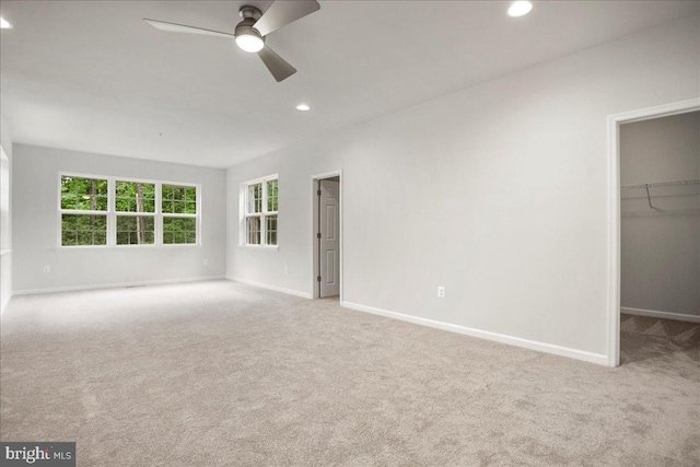 unfurnished bedroom featuring a spacious closet, a closet, ceiling fan, and light carpet