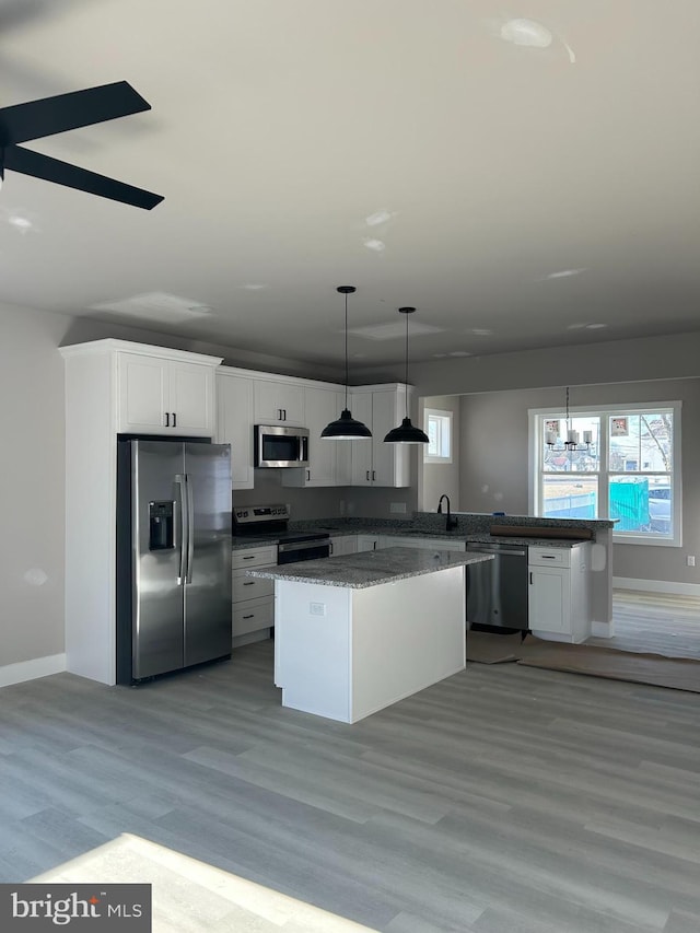 kitchen with appliances with stainless steel finishes, dark stone countertops, hanging light fixtures, light hardwood / wood-style floors, and white cabinets