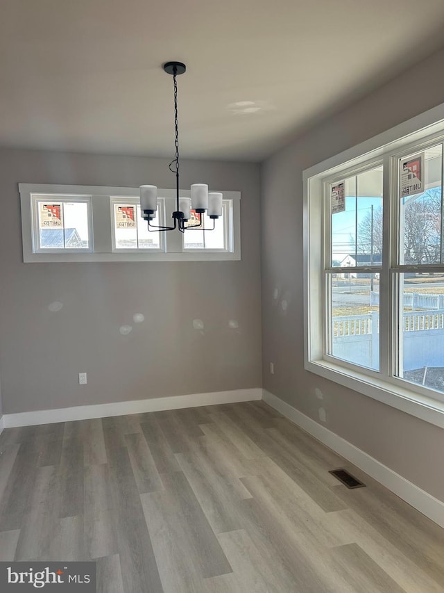 unfurnished dining area featuring an inviting chandelier and light hardwood / wood-style flooring