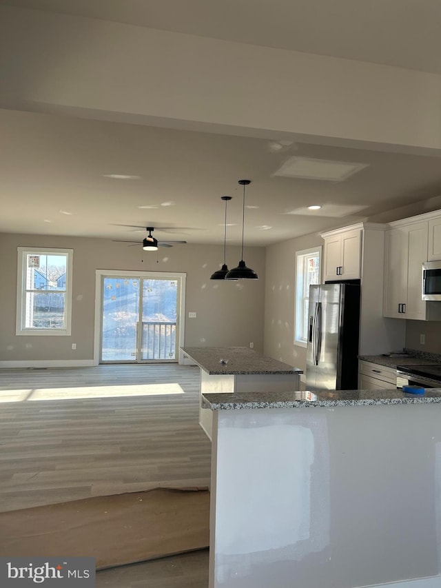 kitchen with pendant lighting, appliances with stainless steel finishes, white cabinetry, light stone counters, and light wood-type flooring