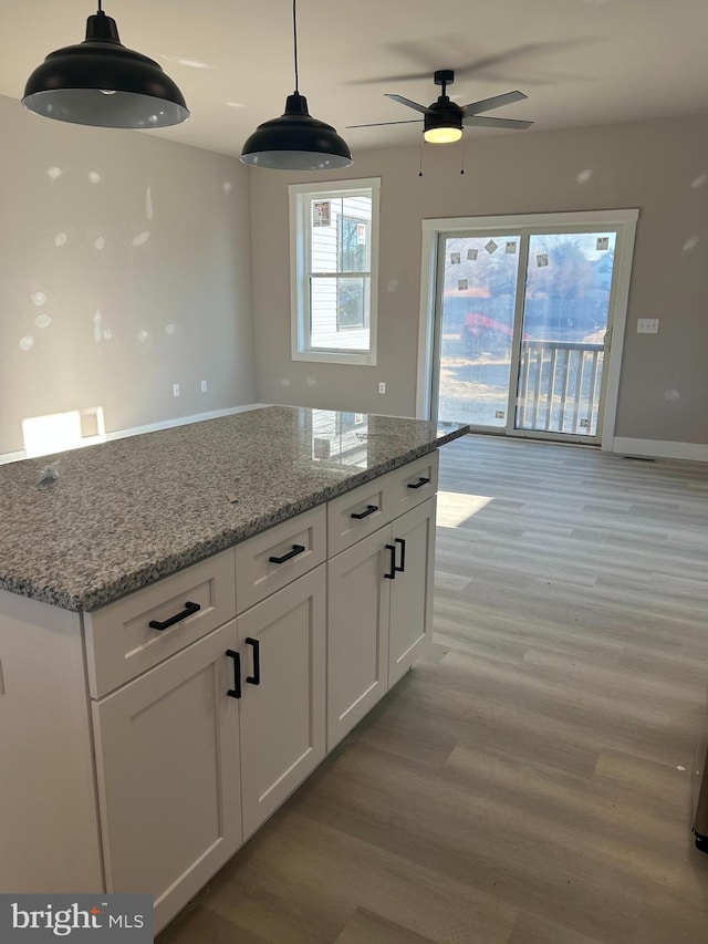 kitchen with white cabinetry, hanging light fixtures, light stone countertops, and light wood-type flooring