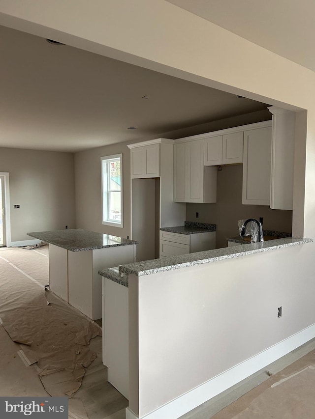 kitchen featuring kitchen peninsula, white cabinetry, a center island, and stone countertops