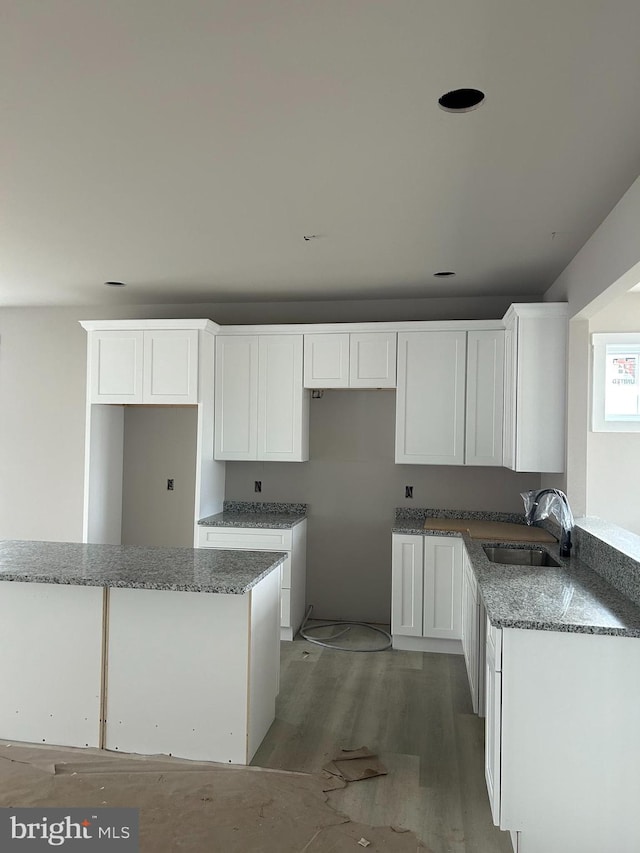 kitchen featuring sink, light hardwood / wood-style flooring, white cabinets, and stone counters