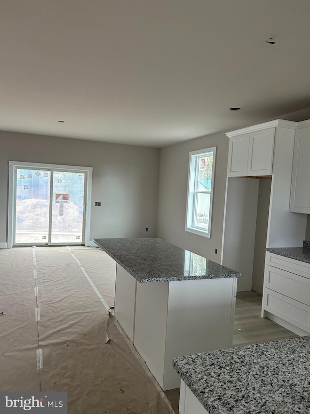 kitchen with a kitchen island, white cabinets, and dark stone counters