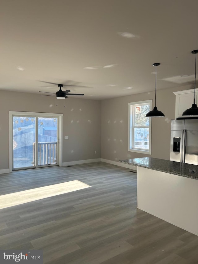 kitchen featuring dark wood-type flooring, decorative light fixtures, stainless steel fridge, dark stone counters, and white cabinets