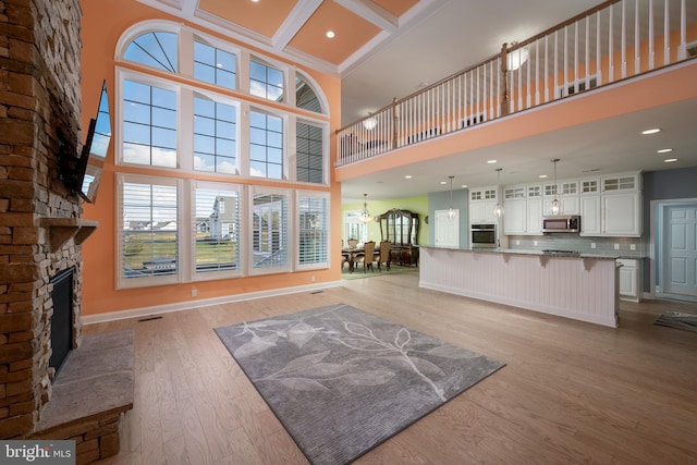 unfurnished living room featuring a high ceiling, coffered ceiling, a stone fireplace, light hardwood / wood-style flooring, and beamed ceiling