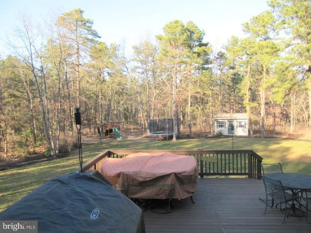 deck featuring a yard, a trampoline, a playground, and a storage unit