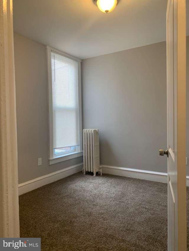 unfurnished room with dark colored carpet and radiator heating unit